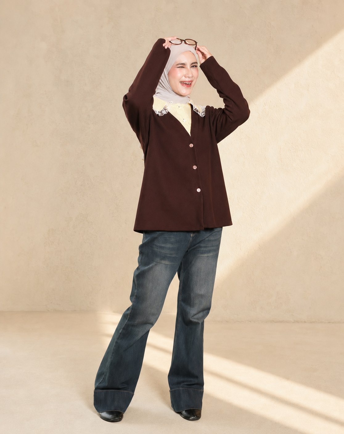 Model berhijab dengan atasan cokelat dan denim dalam pose ceria
