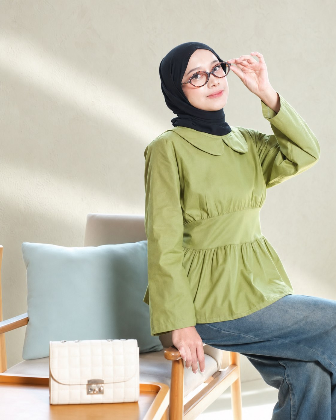 Model berhijab hitam mengenakan atasan hijau sage dan celana denim