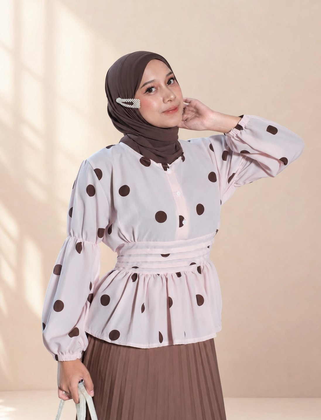 Model berhijab cokelat mengenakan atasan merah muda bermotif polkadot