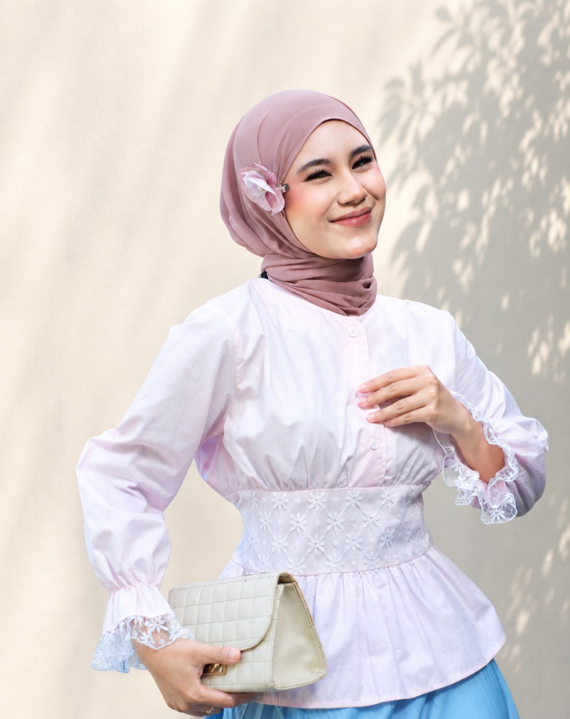 Model berhijab merah muda mengenakan atasan putih beraksen renda